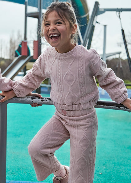 Child in pink cable knit outfit playing on playground equipment