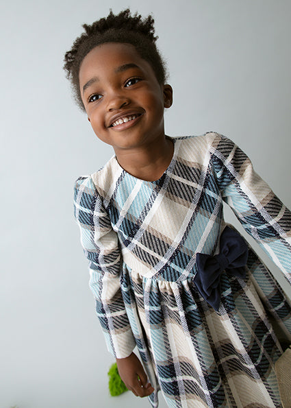 Child wearing a plaid dress with a white background