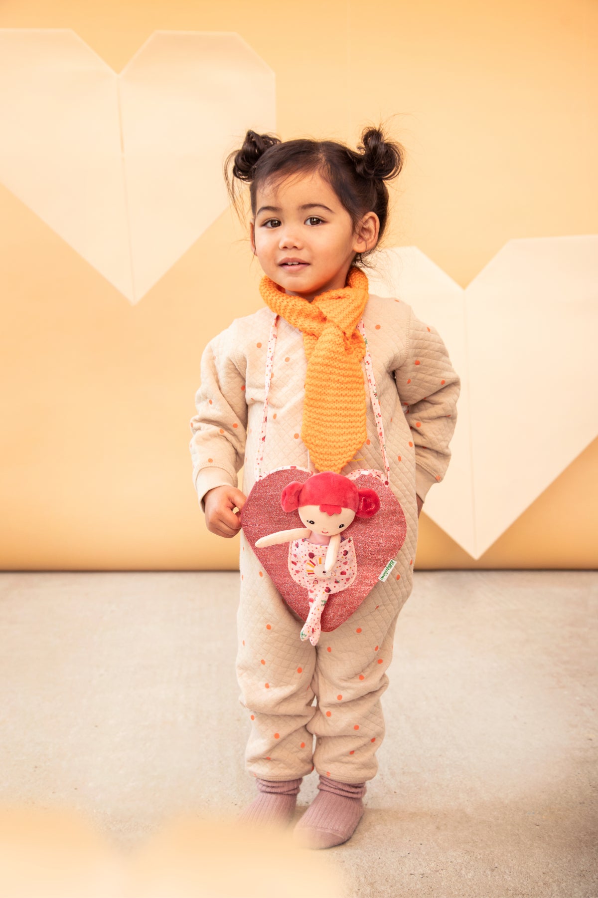 Aline mini fabric doll with deep pink hair, pink top and patterned leggings sitting inside a heart‑shaped children’s bag with unicorn pocket and patterned strap.
