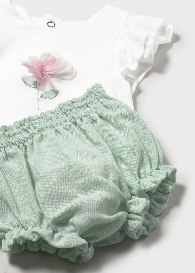 Baby white ruffle‑sleeve top with floral detail and mint green bloomer shorts.