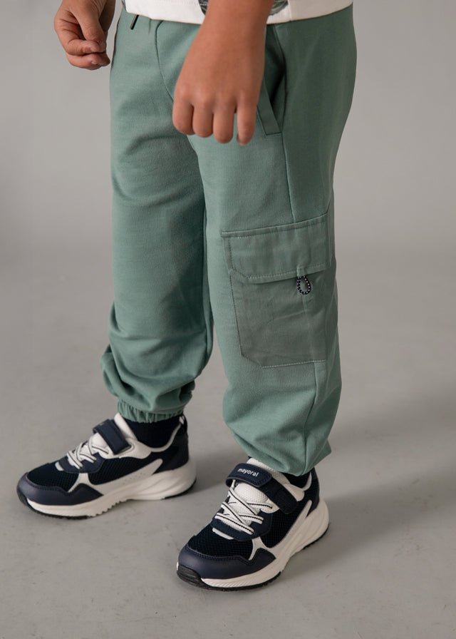Green jogger pants with elastic waistband, black drawstring, side pockets, and cargo flap pocket, styled for kids’ casual summer wear.