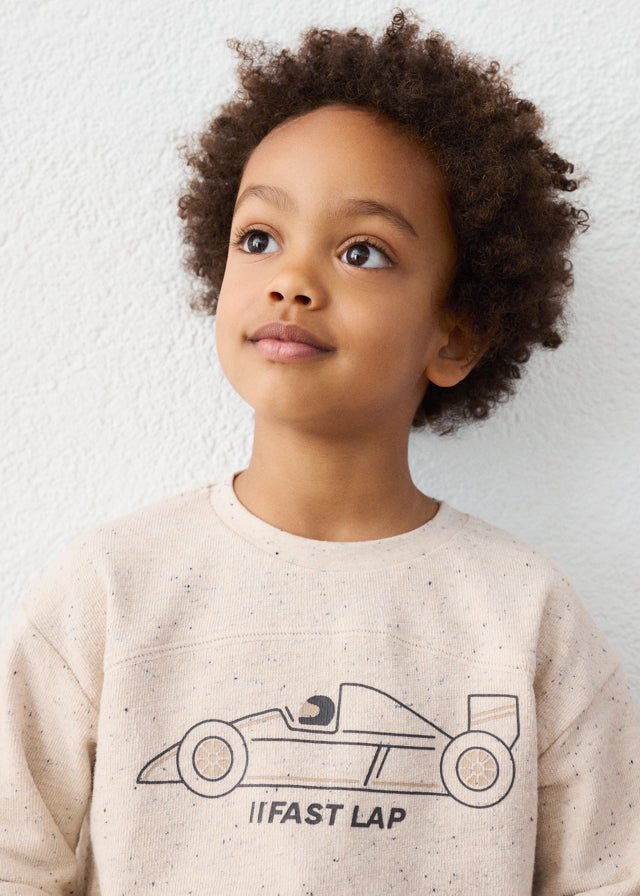 Child wearing a beige sweatshirt with a race car graphic and text against a white background