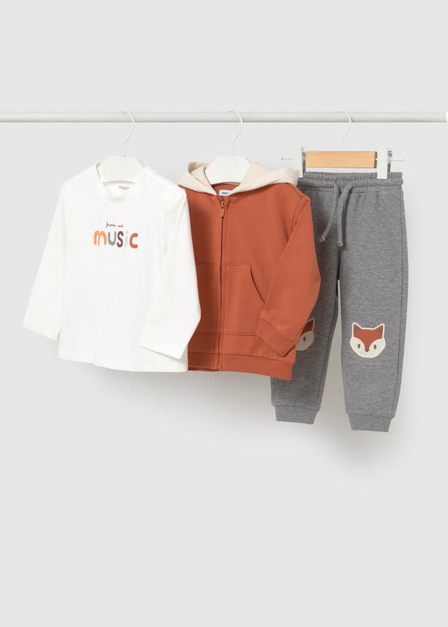 Baby boy three‑piece tracksuit with fox‑red hoodie, printed T‑shirt and grey trousers featuring fox faces on the knees.

