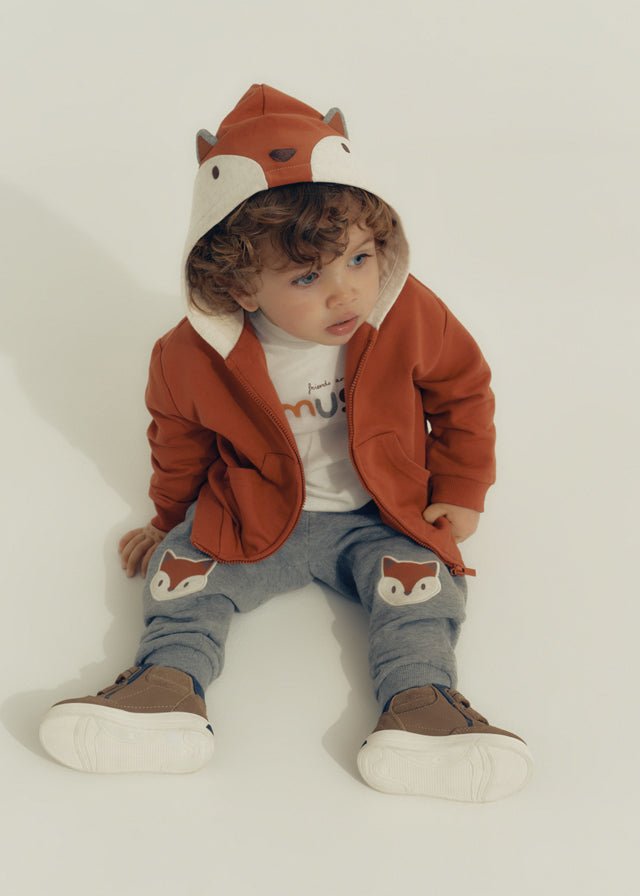 Baby boy three‑piece tracksuit with fox‑red hoodie, printed T‑shirt and grey trousers featuring fox faces on the knees.

