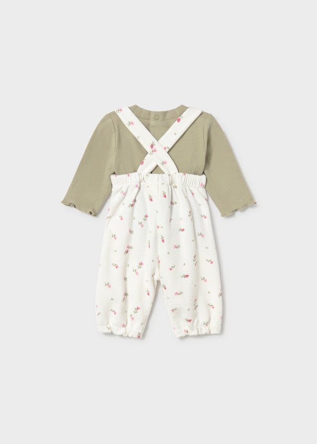 Children's outfit with green long-sleeve shirt and white floral overalls on a light gray background