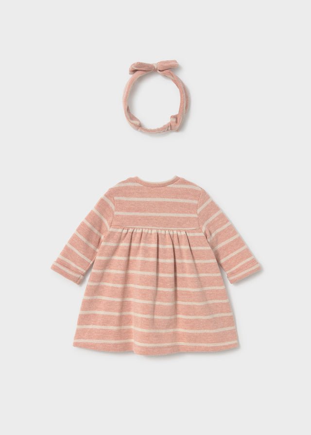 A baby girl's long-sleeve dress in a dusty pink and cream horizontal stripe pattern, shown with a matching fabric bow headband on a light gray background.