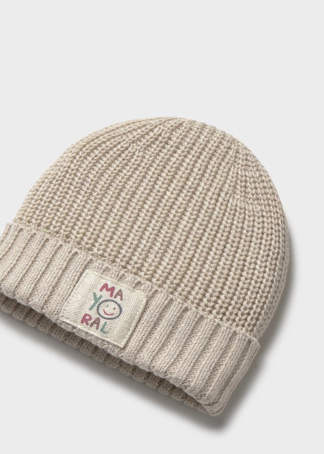 Beige knit beanie with a label on a light gray background