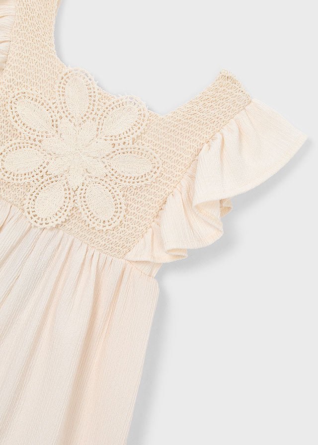 Girls’ cream romper with ruffled shoulders and crochet floral front panel, lightweight and summery.