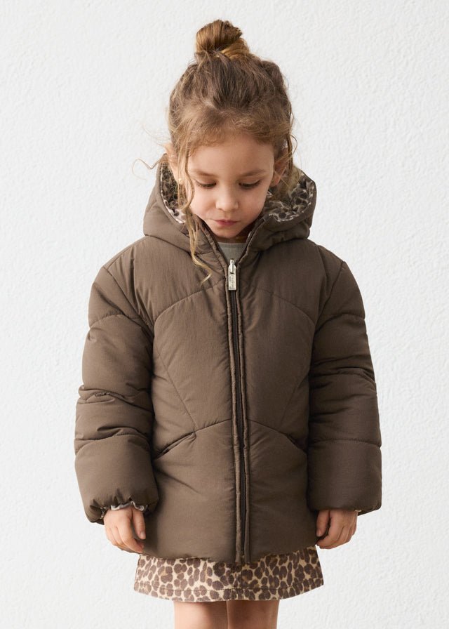 Young girl wearing a brown puffer jacket with leopard print trim on a white background