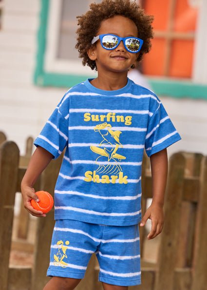 Mayoral Blue and white tie dye striped boys’ shorts with elastic waistband and yellow graphic of a surfing shark wearing sunglasses.