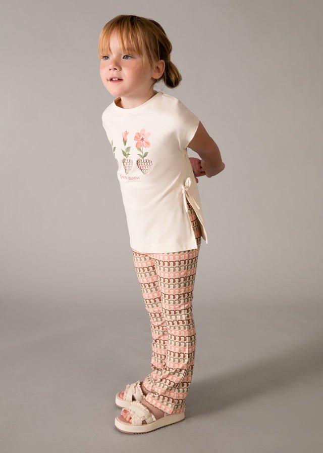Girls’ two-piece holiday outfit with beige printed top and flared patterned trousers in soft pink, green, and beige.