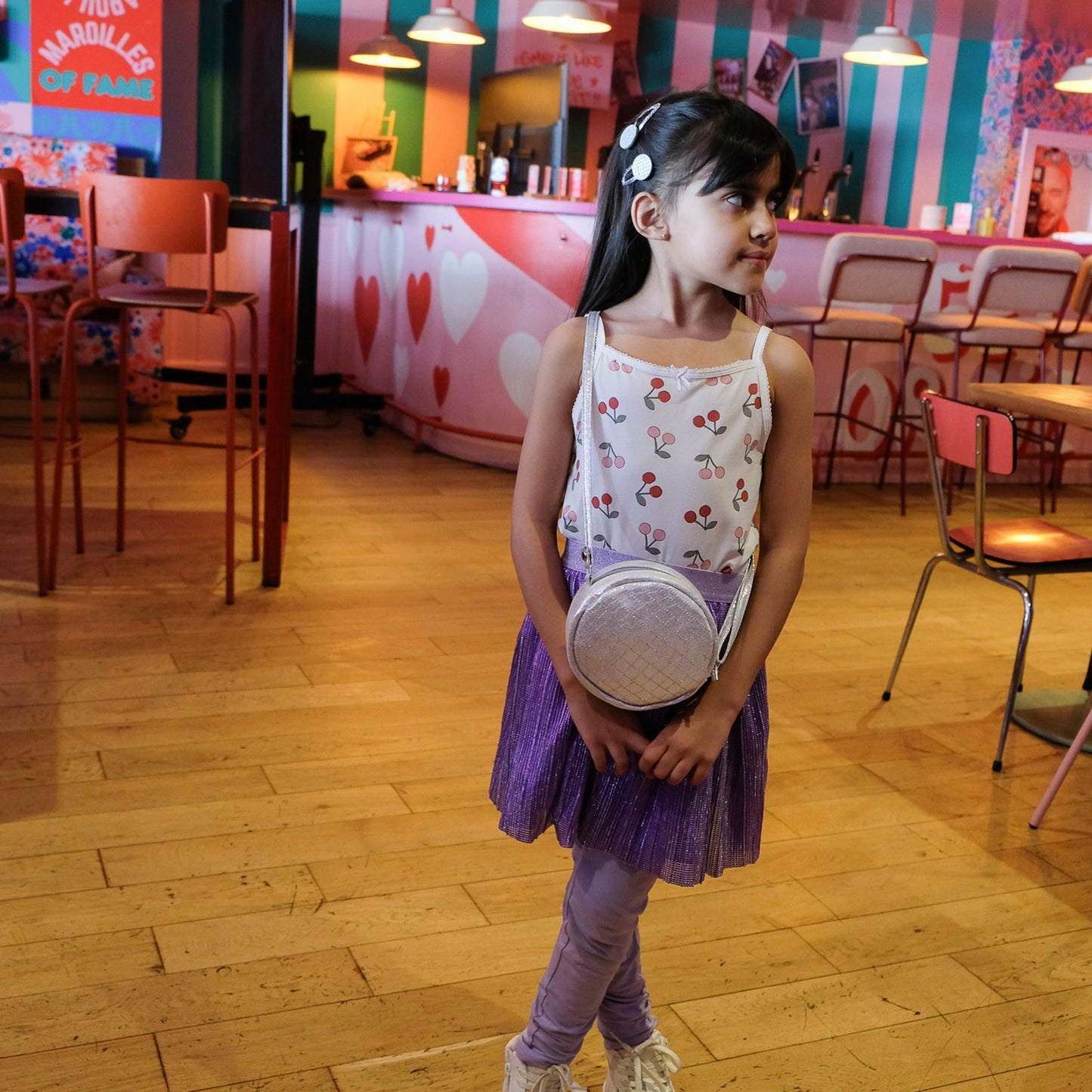Young girl in a colorful indoor setting holding a Rockahula disco ball small bag