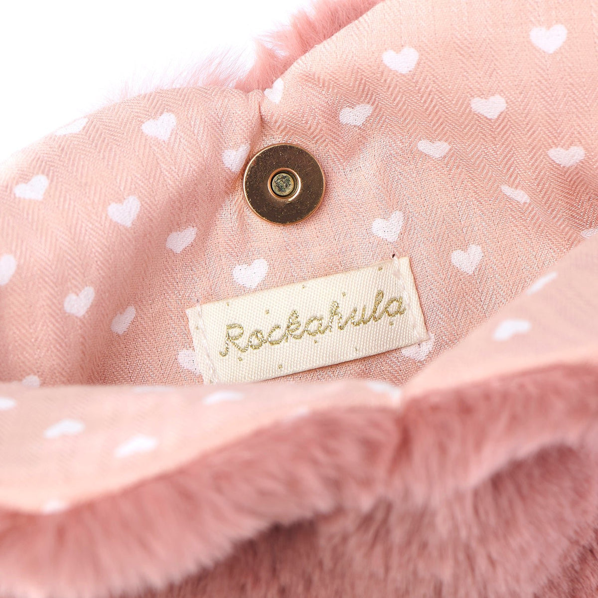 Inside Rockahula pink fluffy heart bag. Close-up of inside a pink fabric with heart patterns and a 'Rockahula' label.