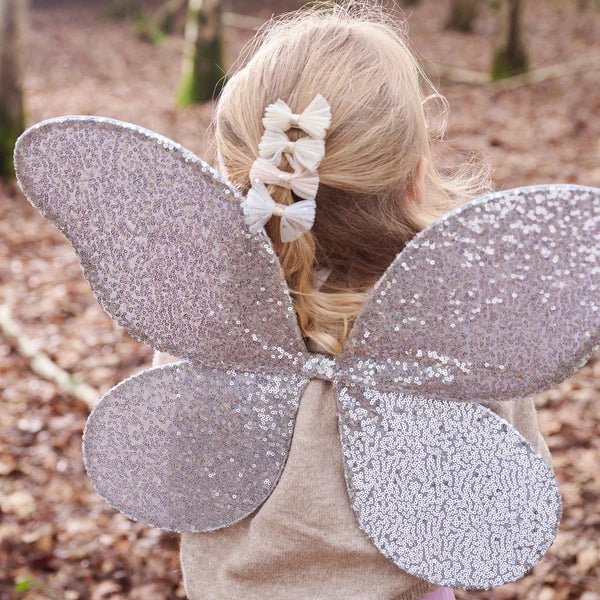 Child wearing silver sequin fairy wings outdoors and Shimmer tulle bow hair clips.